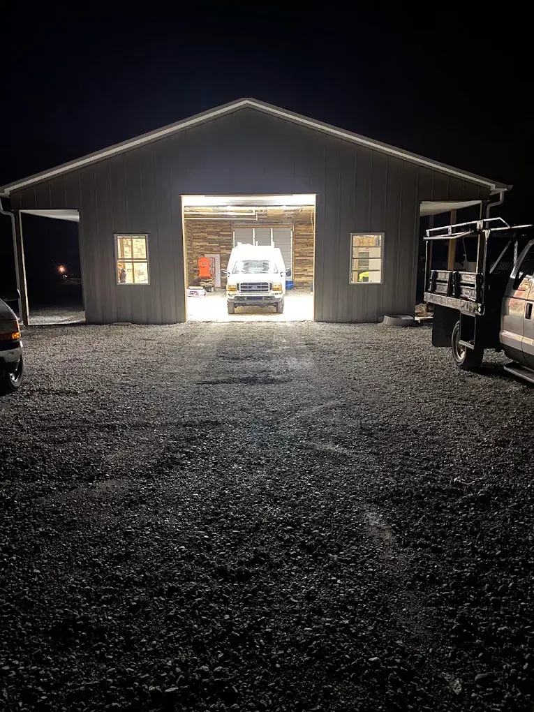 Nighttime view of a gravel lot and open garage with bright lights and a truck inside.