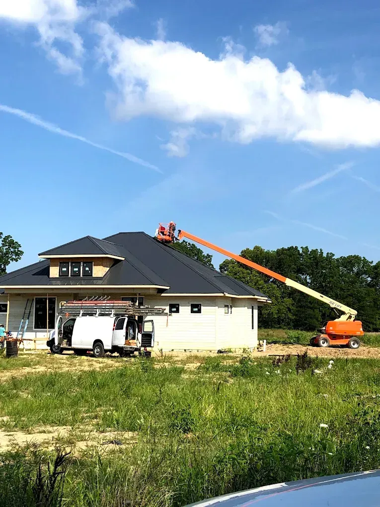 Orange boom lift workers on a house roof during construction under a blue sky