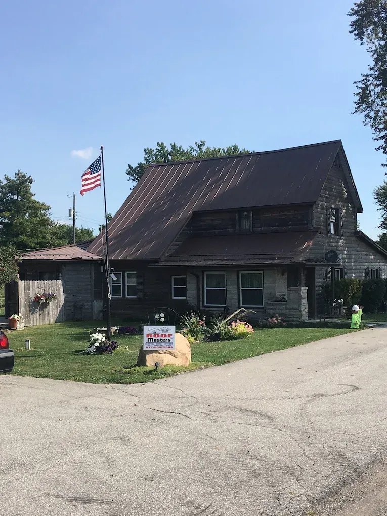 Small dark house with American flag, roadside lawn signs, and a paved driveway on a sunny day
