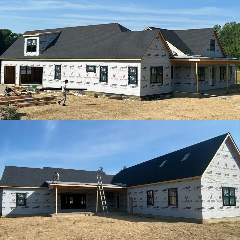 New house under construction with white siding, dark roof, and a worker in the front yard