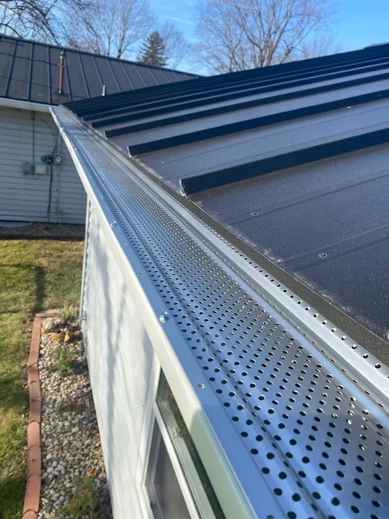 Black rain gutter and downspout on beige house under gray shingled roof