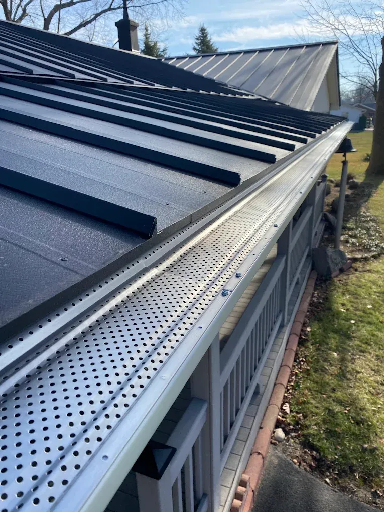 Black rain gutter and downspout on beige house under gray shingled roof