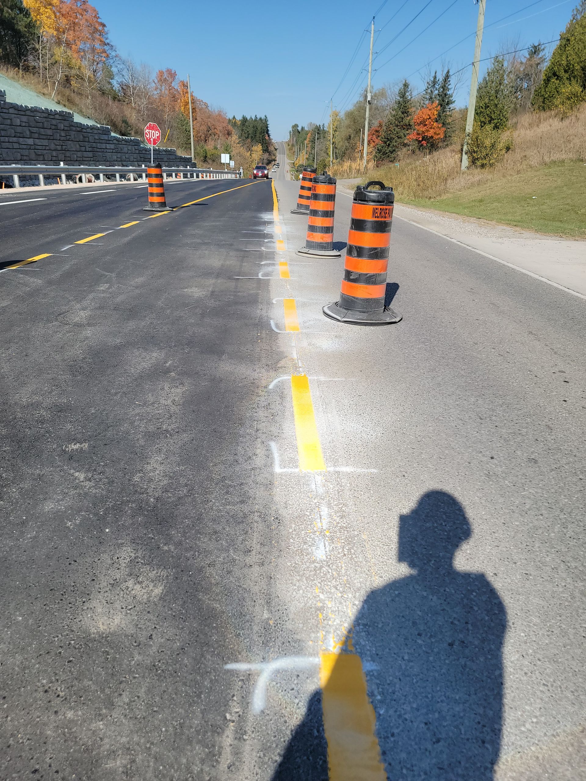 Road under construction with orange cones and yellow lines. Shadow of person taking photo on the road.