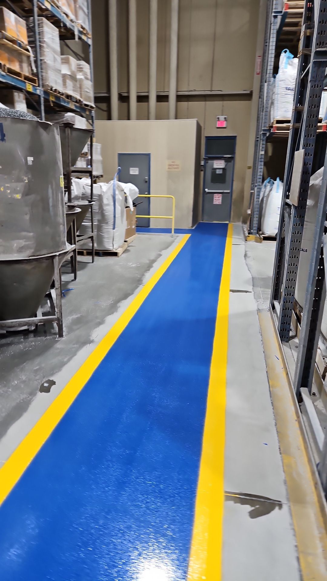 Warehouse aisle with blue painted floor, yellow borders, and shelving on both sides.