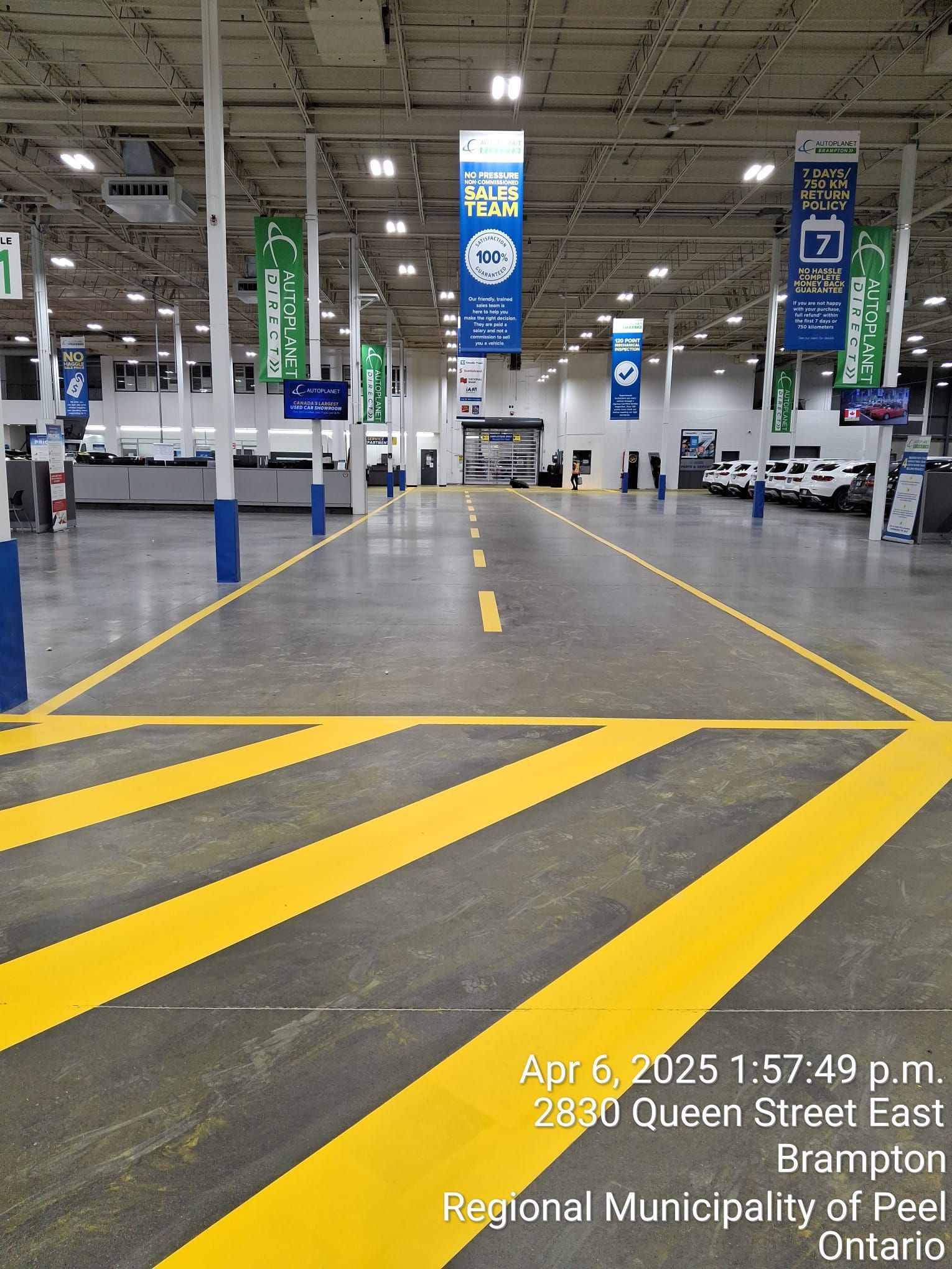 Interior view of an empty warehouse-like space, yellow lane markings, blue support beams, banners, 
