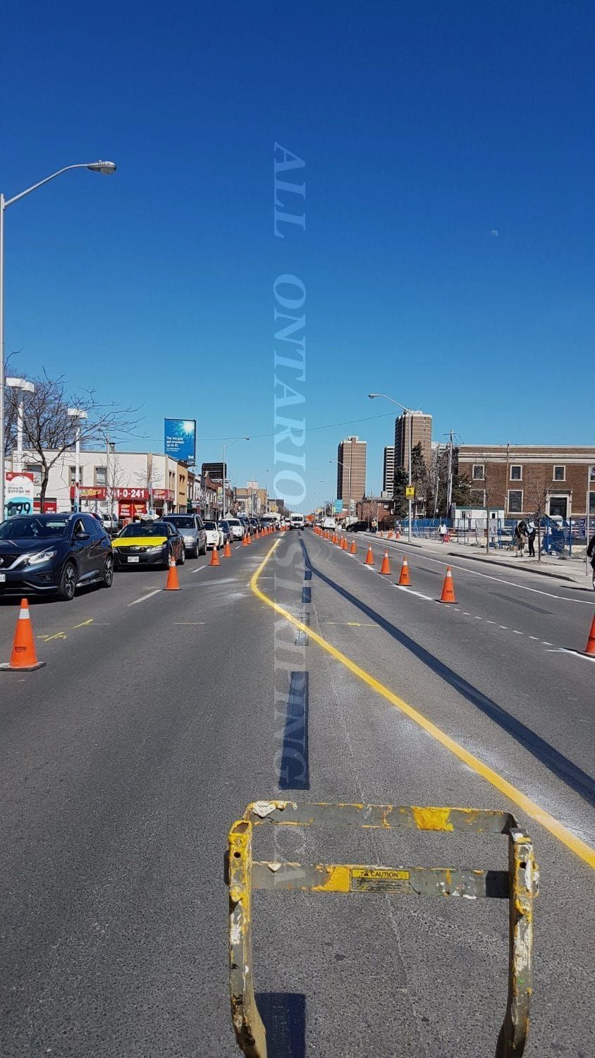 Street under construction with orange cones and yellow lines, blue sky.