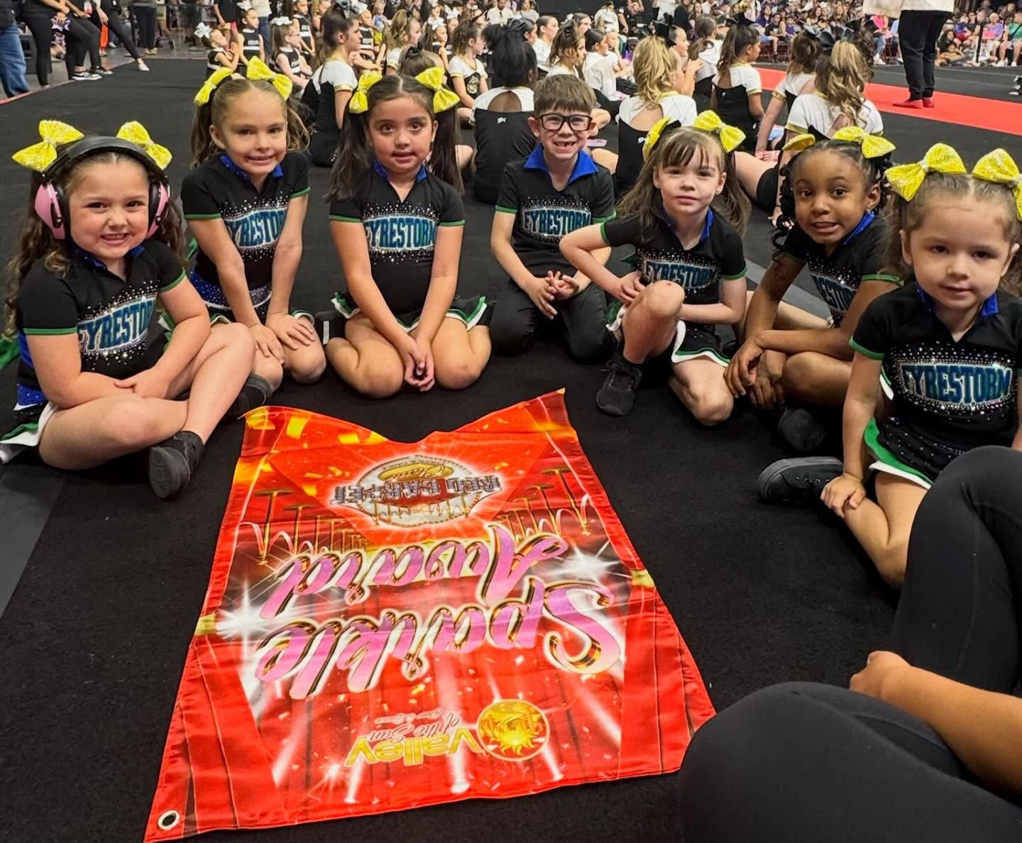 Group of young cheerleaders sitting on the floor around a red banner at a competition