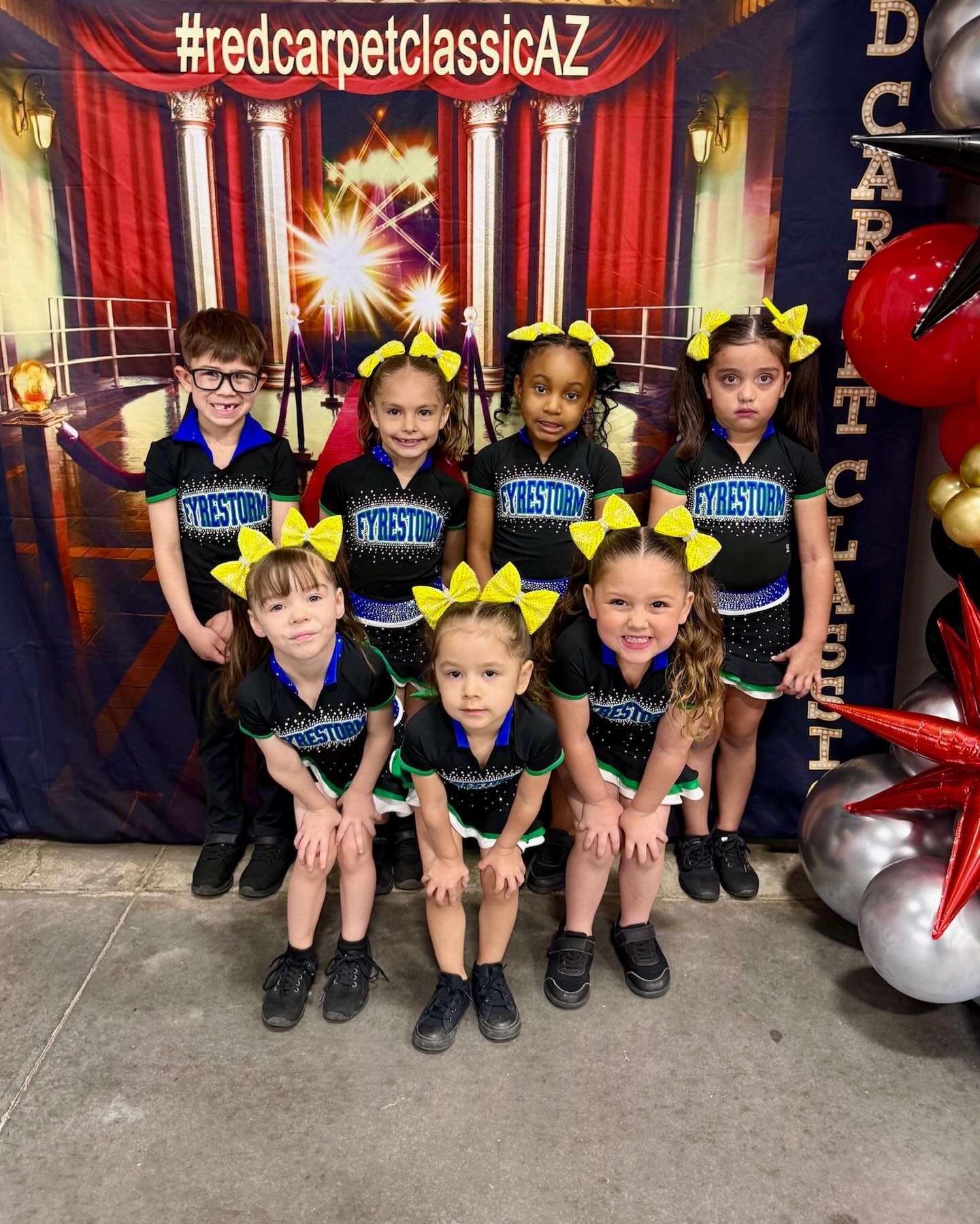 Six children in matching blue and black dance costumes pose in front of a red curtain backdrop.