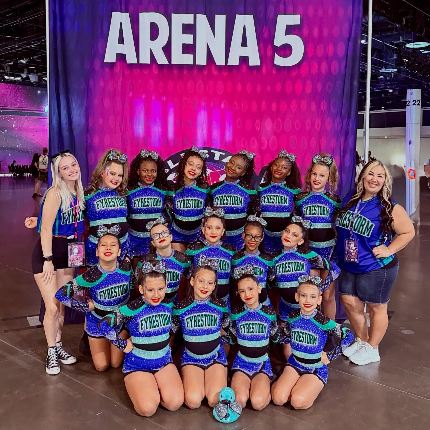Cheer team posing in blue-and-purple uniforms in front of an ARENA 5 sign
