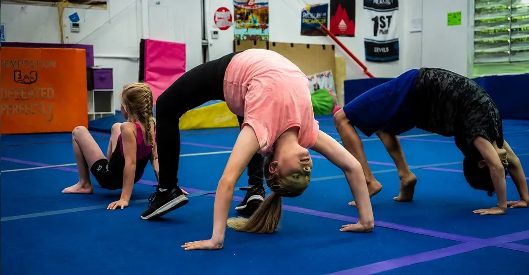Three people doing backbends on blue gym mats in a training studio