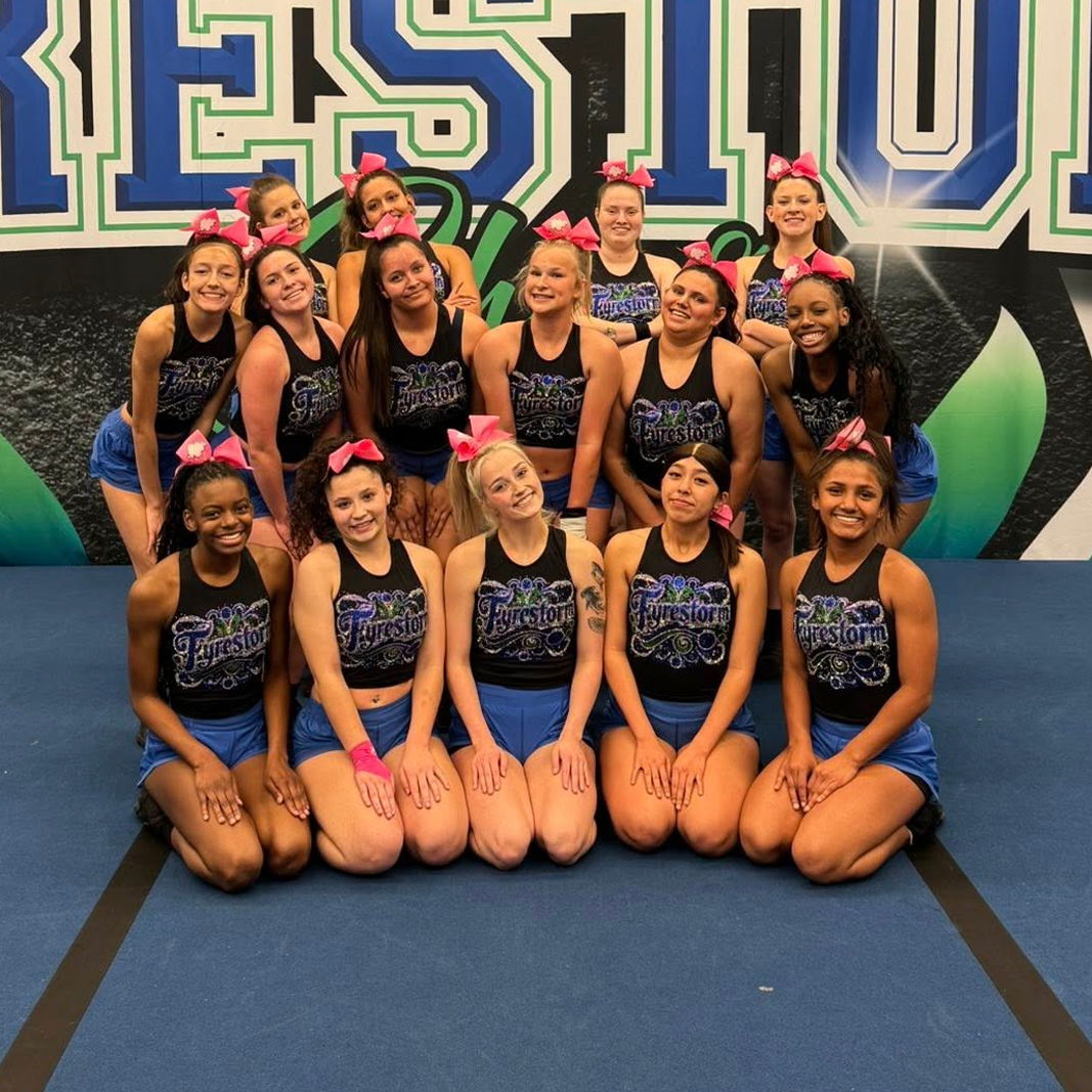 Cheer team posing in blue and black uniforms in front of a large event backdrop.