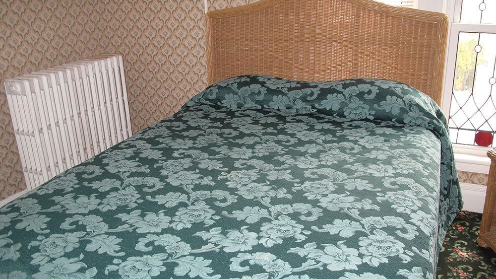 A bed with a green blanket and a wicker headboard