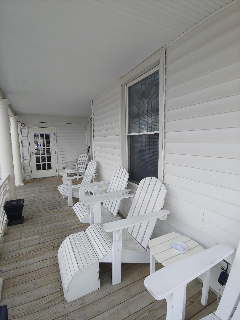 A porch with a lot of white chairs and tables