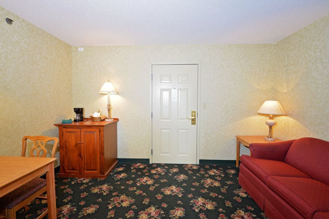 A hotel room with a couch , table , chairs and a door.