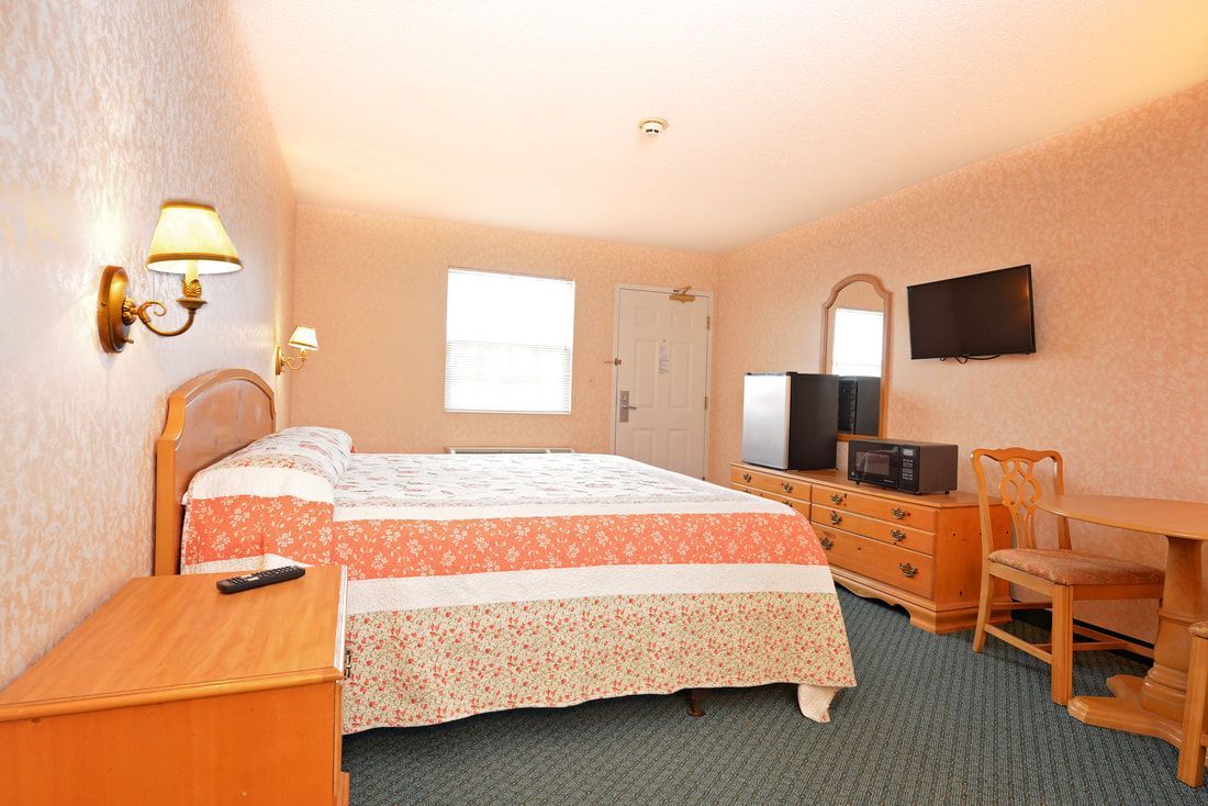 A hotel room with a bed , dresser , chair , table and television.