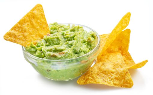 A bowl of guacamole and tortilla chips on a white background