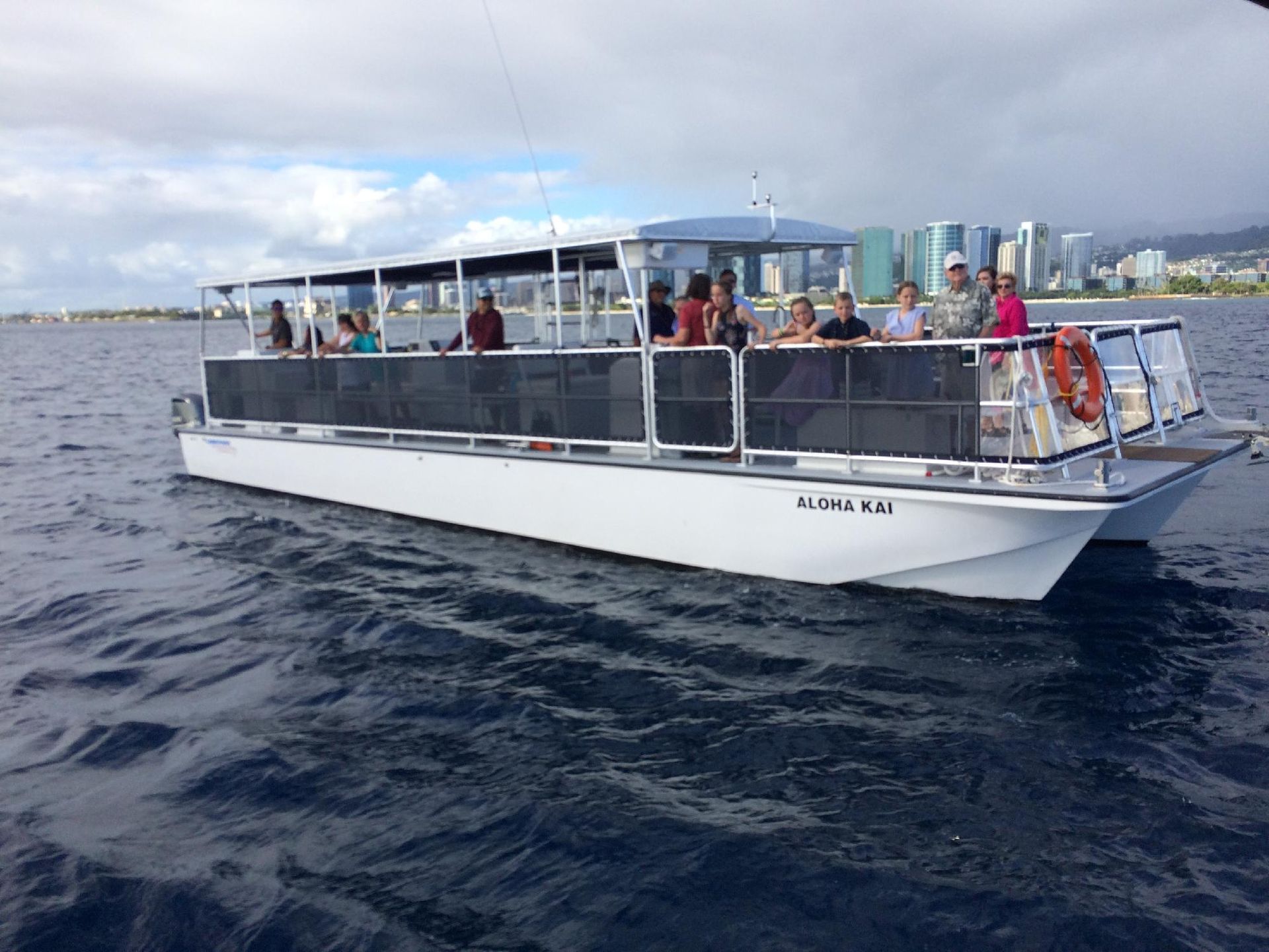 White passenger boat cruising on choppy water near a city skyline under a cloudy sky