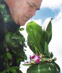 Man leaning in to smell a white flower with green leaves against a blue sky