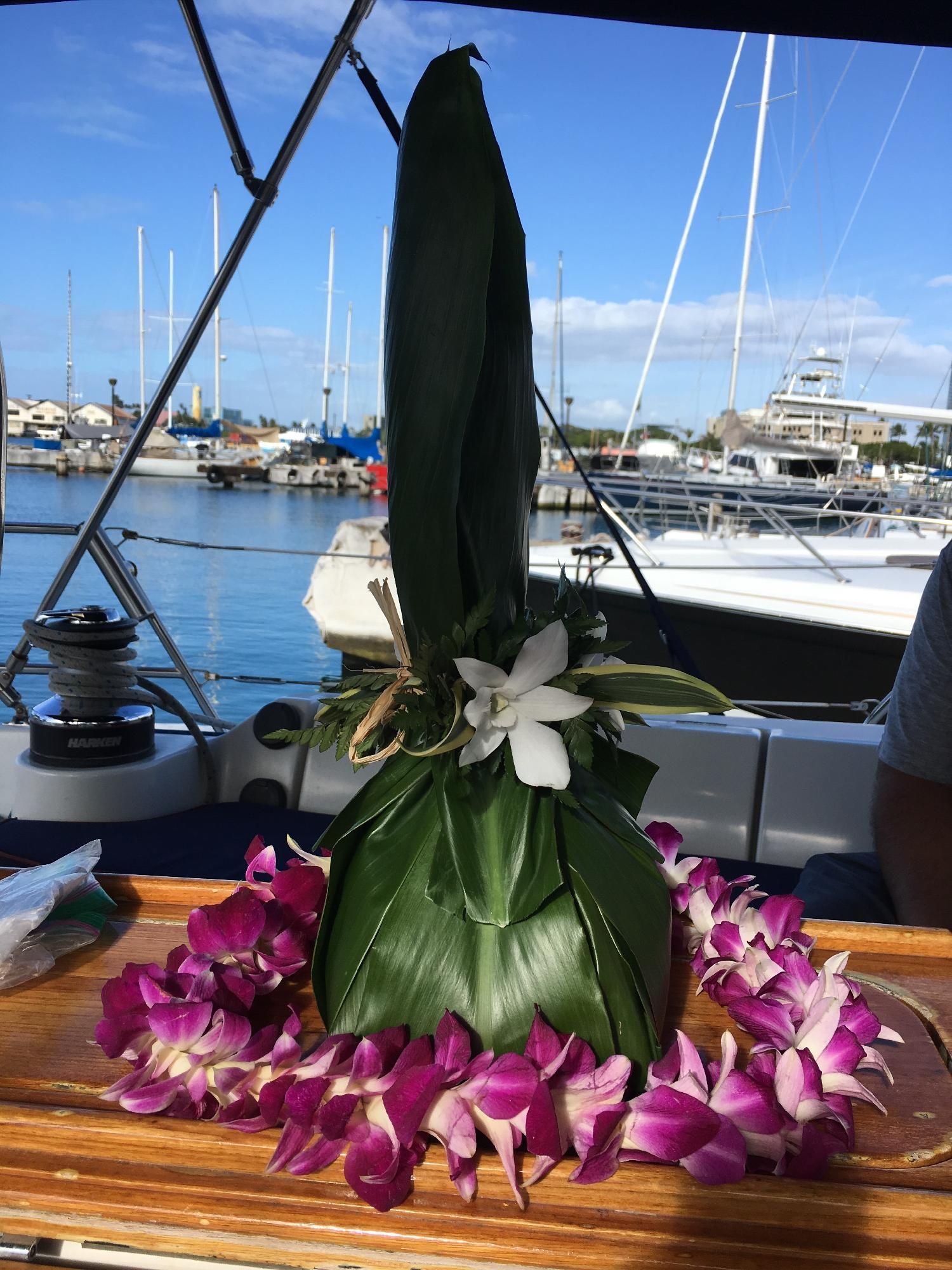 Flower lei wrapped around a wrapped bottle centerpiece on a table by the marina.