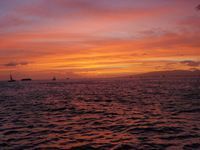 Sunset over a calm ocean with orange and pink sky and distant boats on the horizon