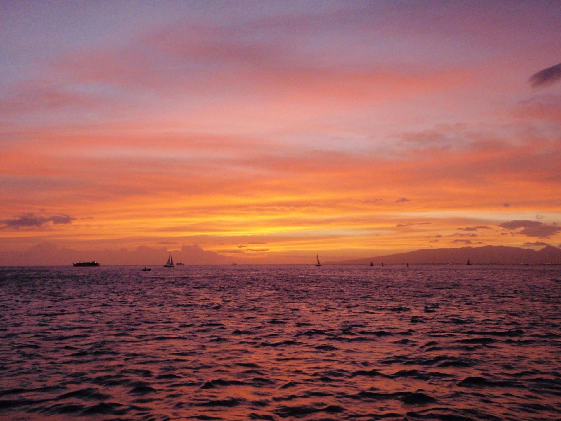 Sunset over a calm ocean with pink and orange sky and a small boat on the horizon