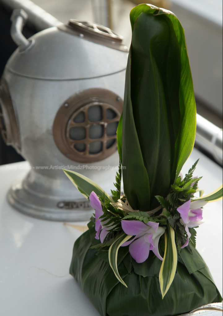 Wrapped green plant arrangement with purple flowers on a table beside a silver kettle