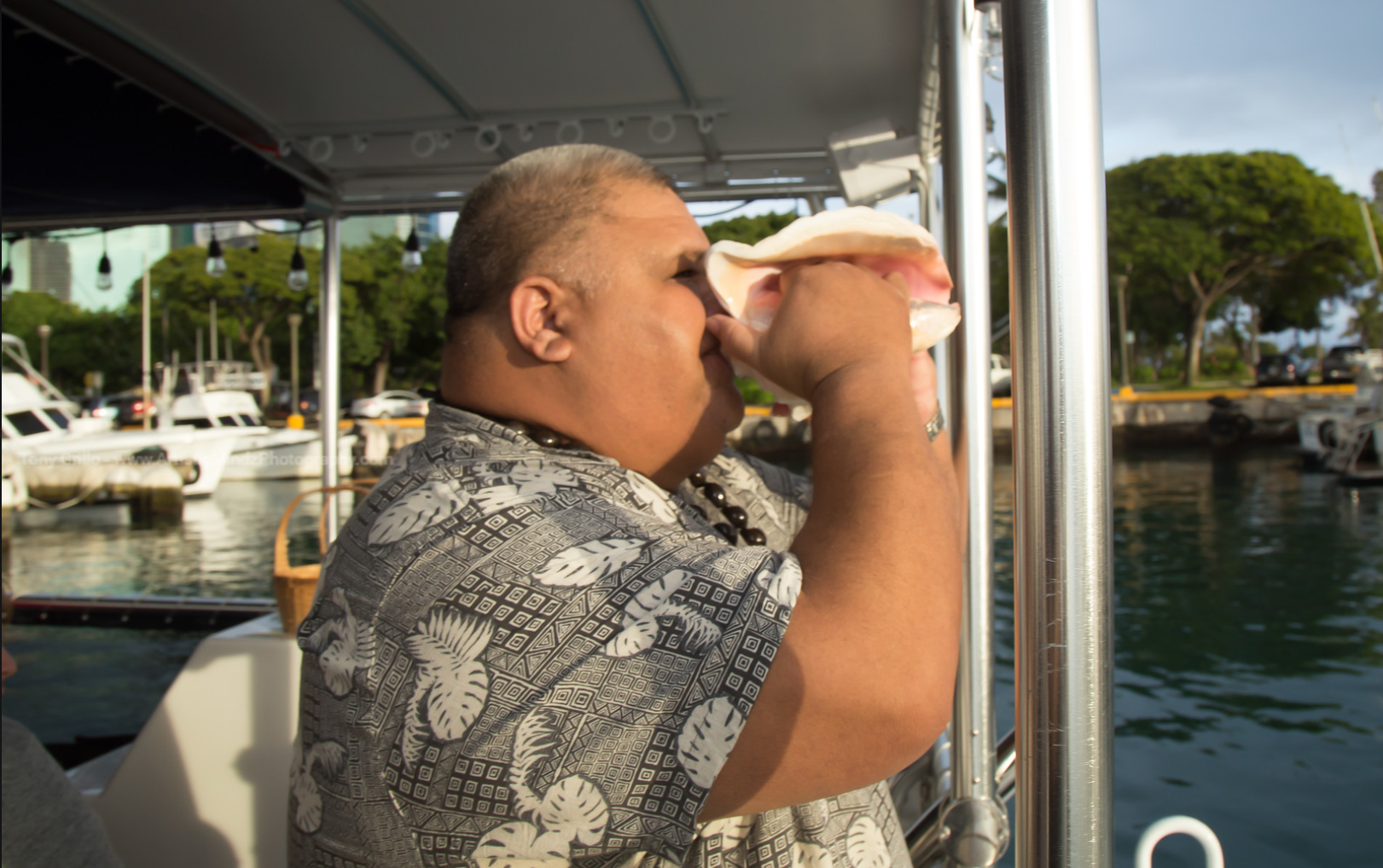 Man on a boat drinks from a cup beside calm marina water and docked boats