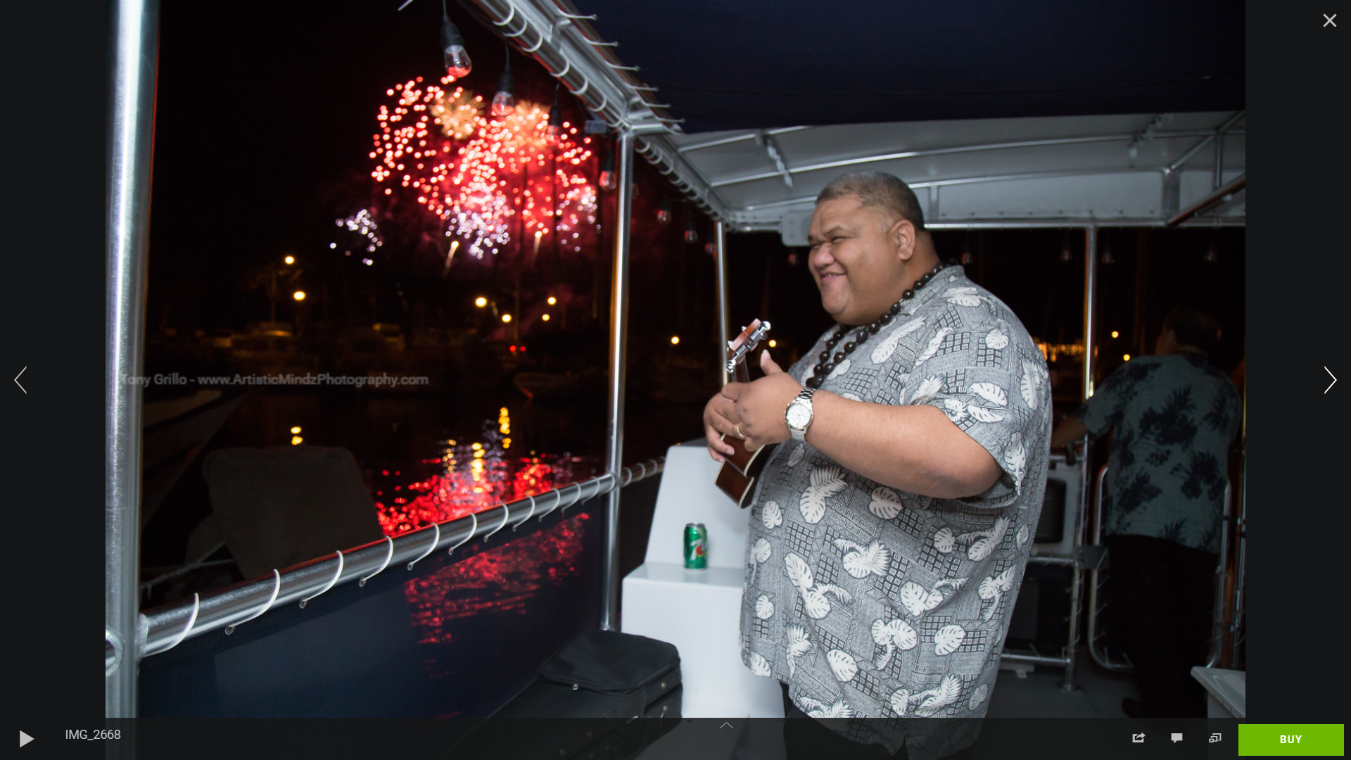 Person standing on a boat deck watching fireworks over the water at night