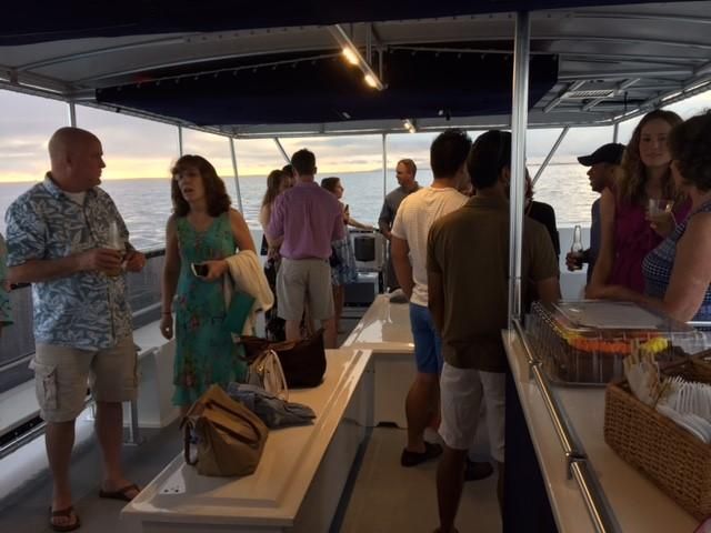 Guests socializing at a yacht buffet with tables, wicker baskets, and ocean views under a canopy