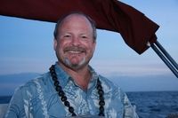Smiling man on a boat at sea during sunset, wearing a blue shirt and lei