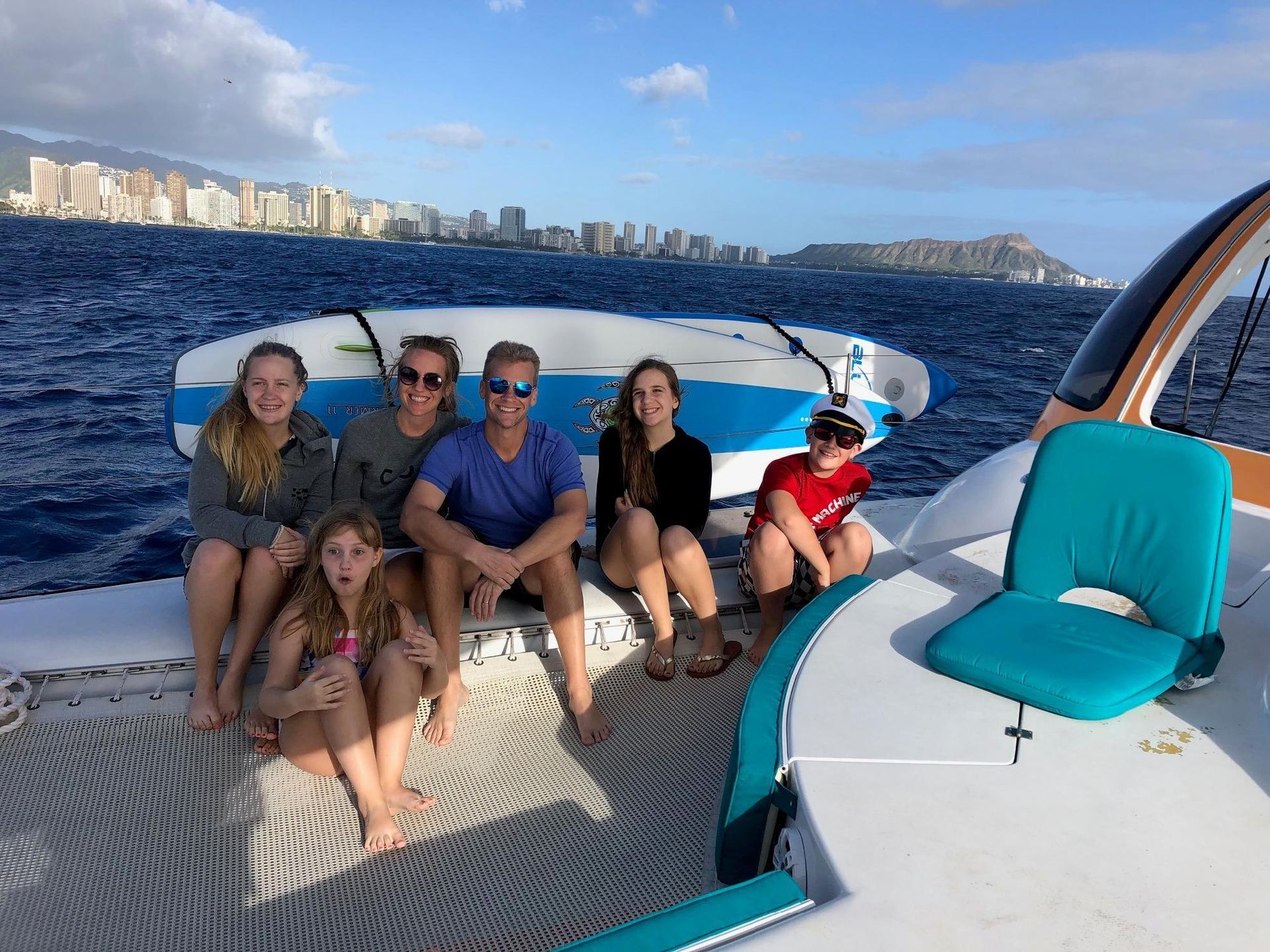 Six people relaxing on a boat at sea, with a city skyline in the background.