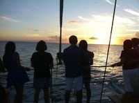 Silhouetted people stand by a railing watching the sunset over the ocean.