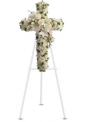White floral cross tribute on an easel, decorated with pale flowers and greenery