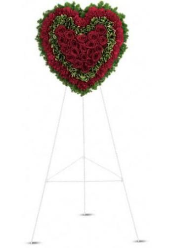 Heart-shaped red and green floral wreath on a white stand with three slender legs