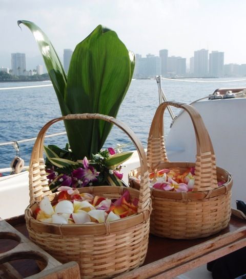 Two wicker baskets of flower garlands and greenery on a boat with a city skyline and water in the background