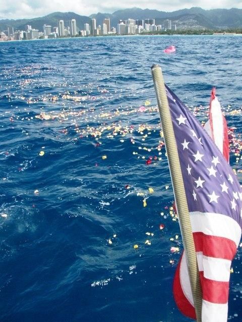 American flag on a boat over blue water with a distant city skyline in the background