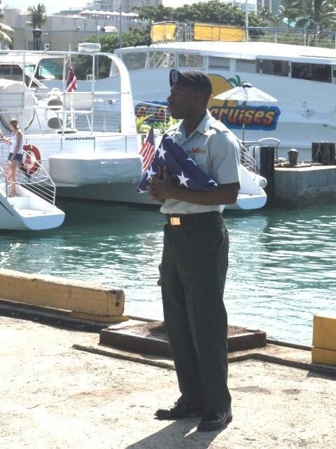Person standing on a dock holding a folded flag, with boats and water in the background.