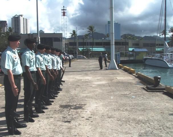 Uniformed people standing in formation along a dock beside water under cloudy skies