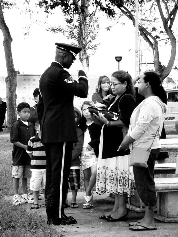 Police officer speaking with a small group outdoors near trees and a fence