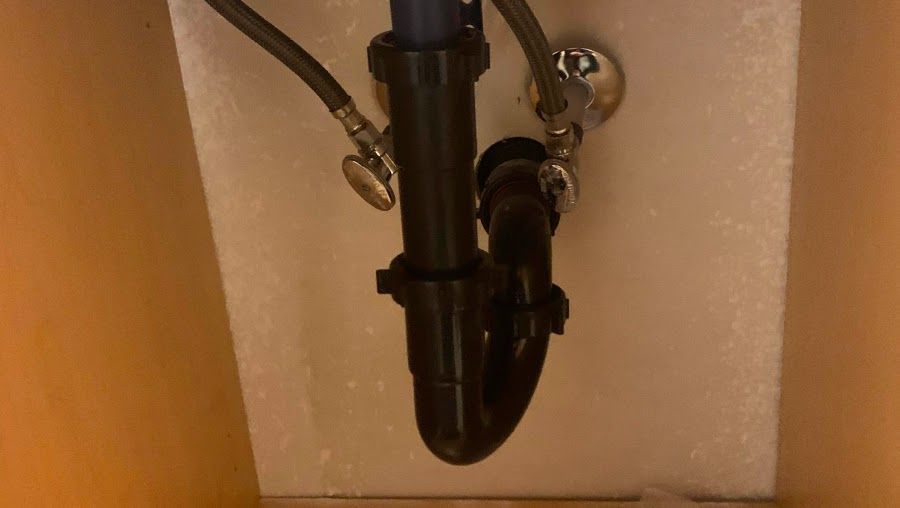 A close up of a sink pipe in a cabinet.