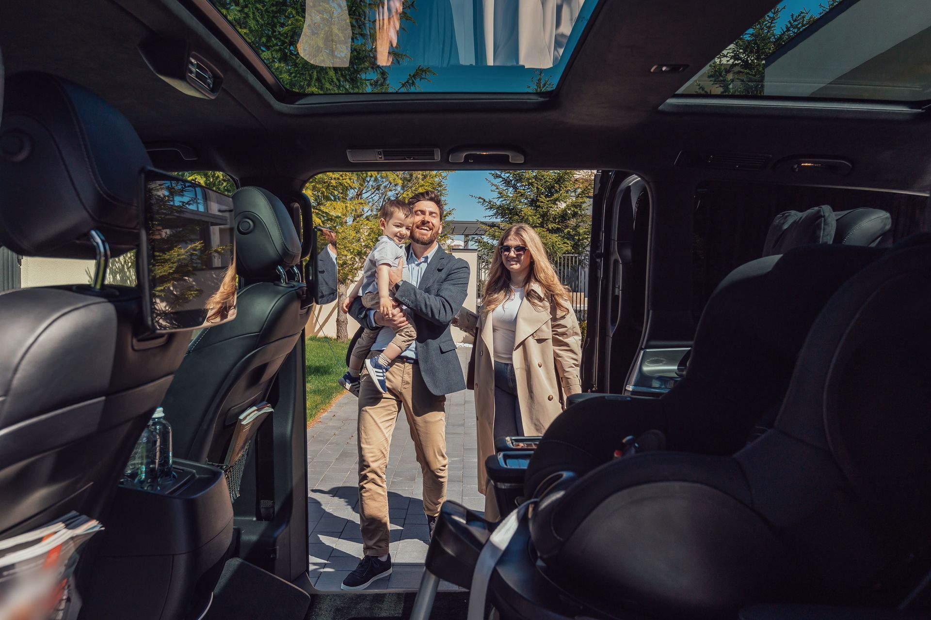 Two people standing beside an open luxury van, smiling in a sunlit street scene