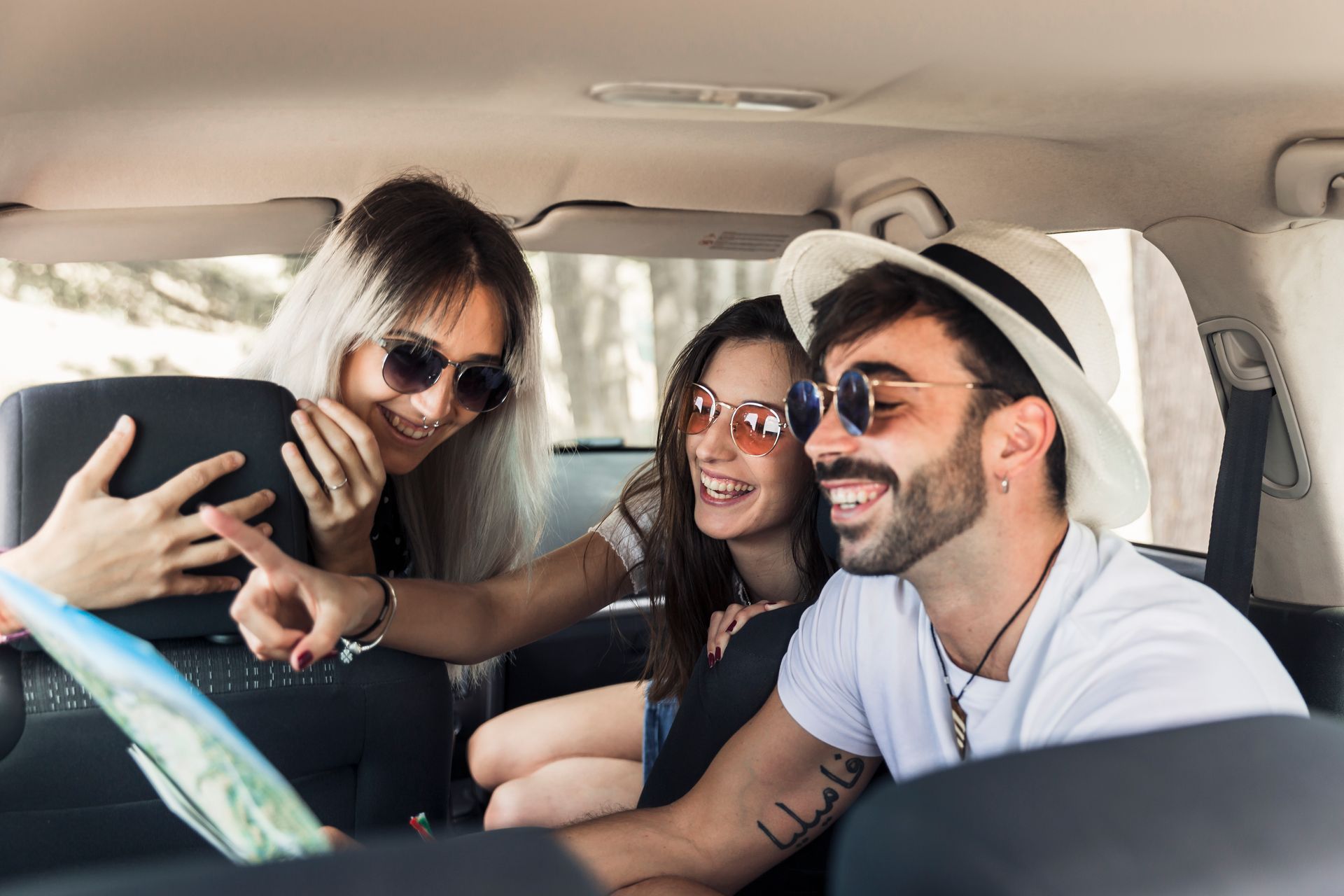 Three friends taking a selfie in a car, smiling and wearing sunglasses