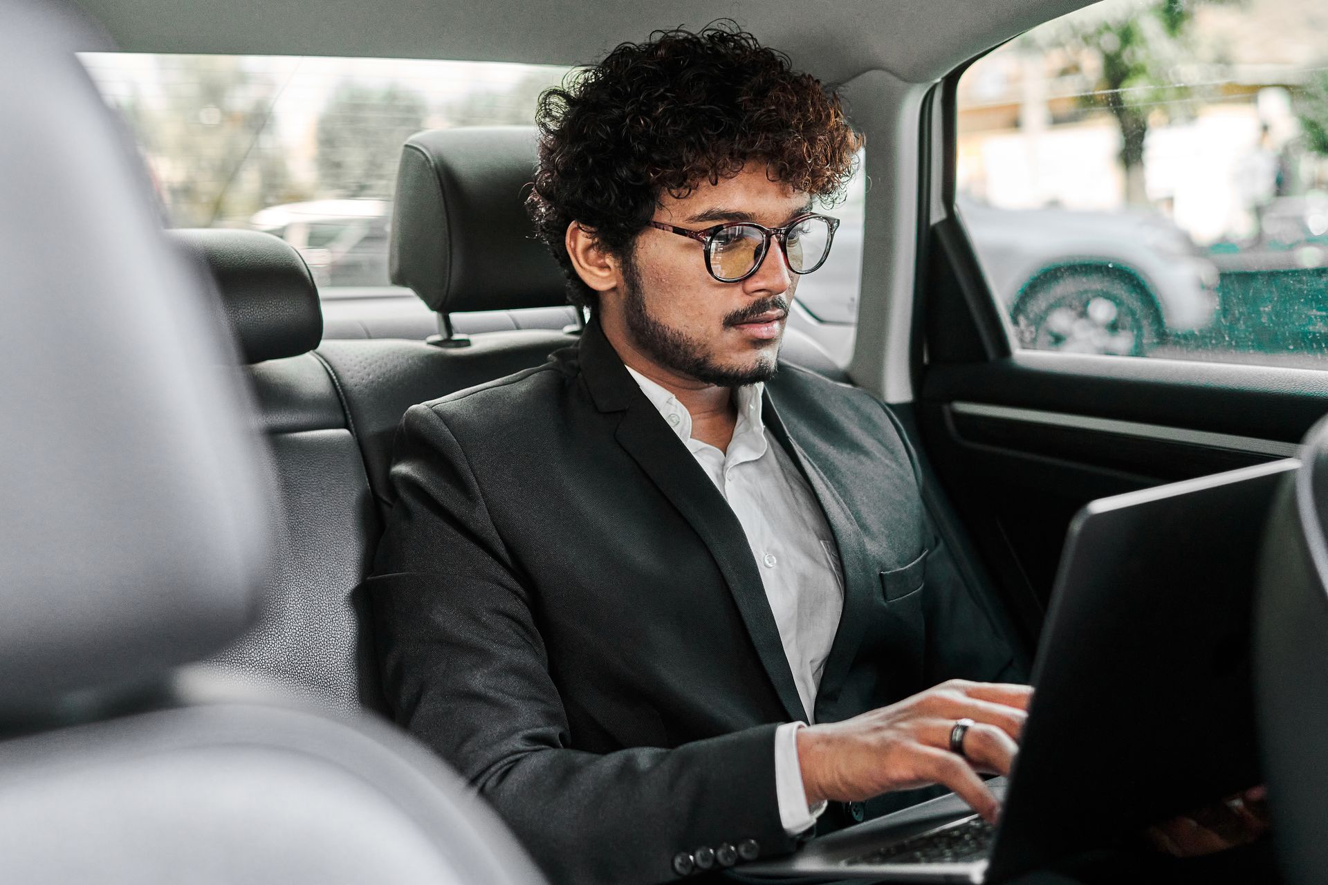 Man in a dark suit using a laptop in the back seat of a car