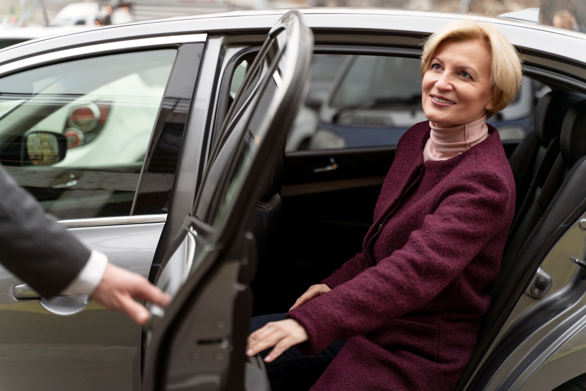 Woman smiling as she gets into a black car while someone opens the door