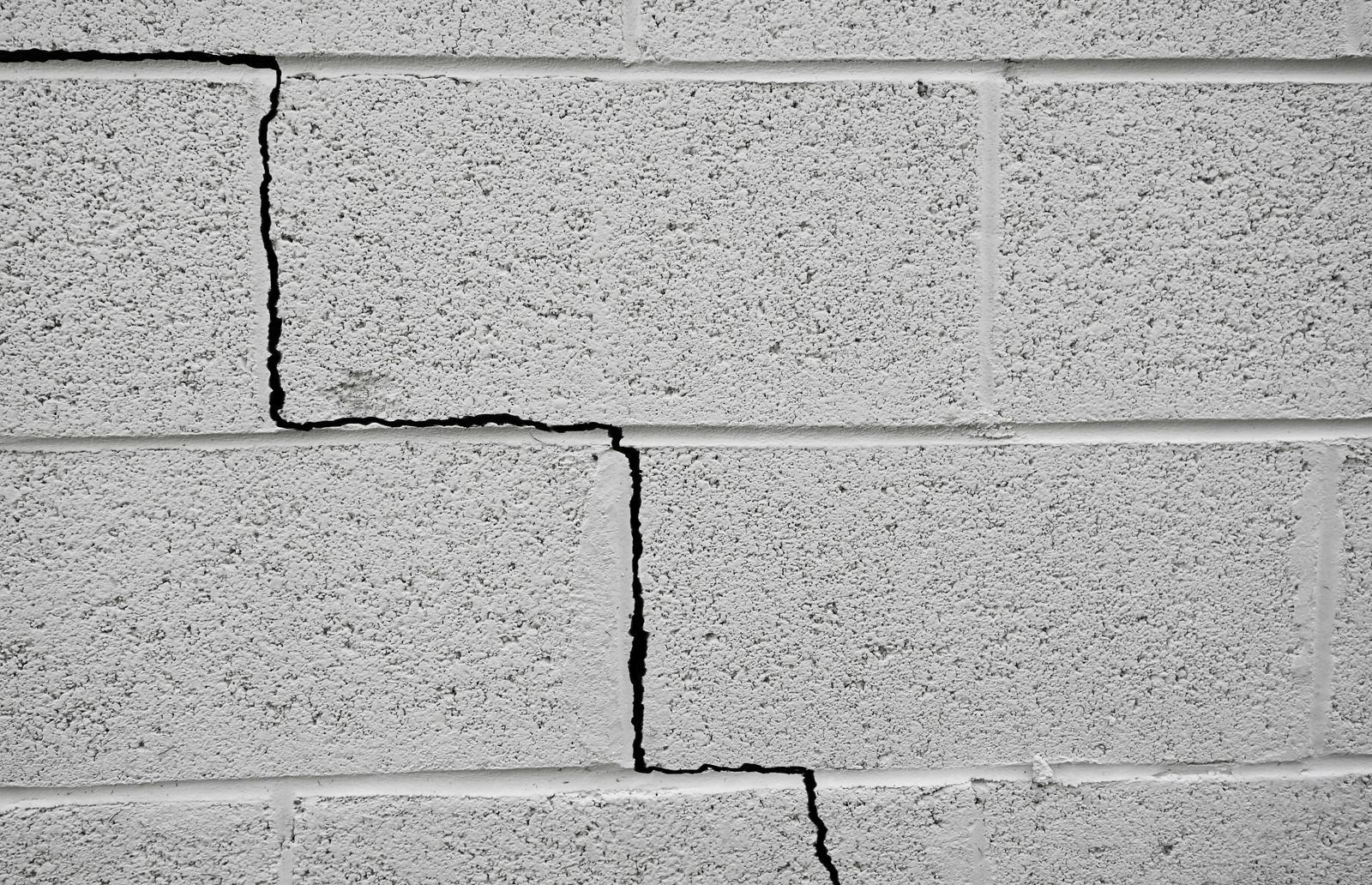 Gray cinder block wall with a zigzag crack running across the blocks