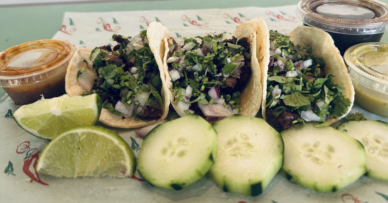 A tray of tacos with lime wedges and various dipping sauces, accompanied by a bottle of Carta Blanca beer.