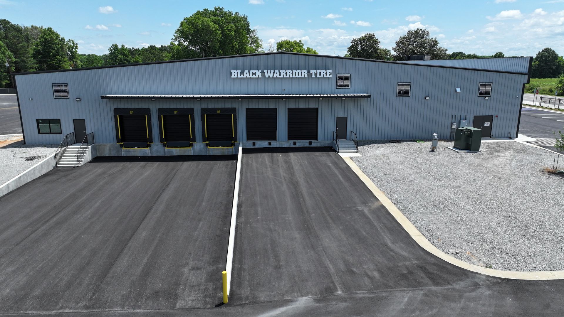 Front view of a gray building labeled “ALBIS CRUSHER LTD,” with a paved driveway and gravel lot