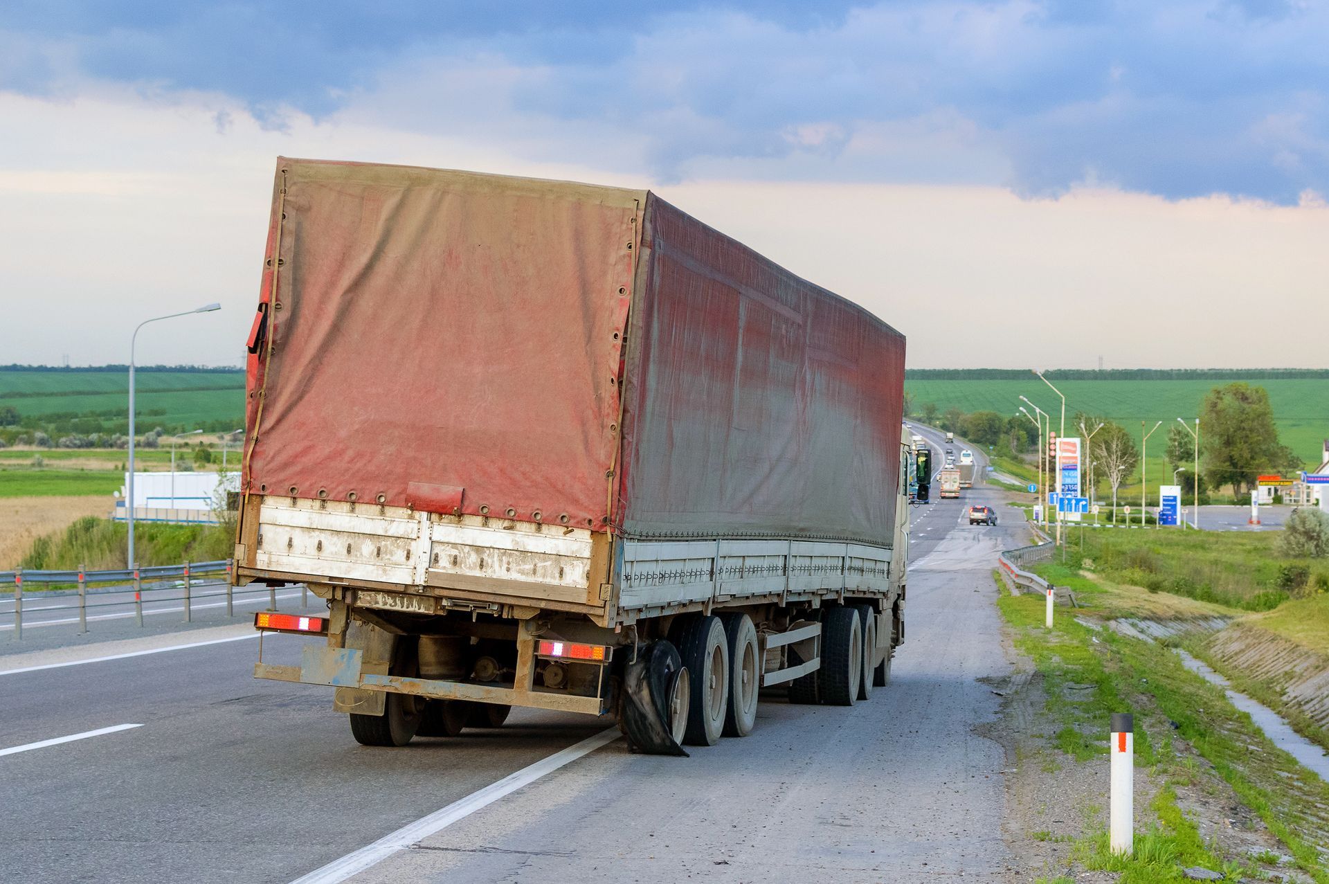 Large tarp-covered semi truck driving on a rural road under a cloudy sky