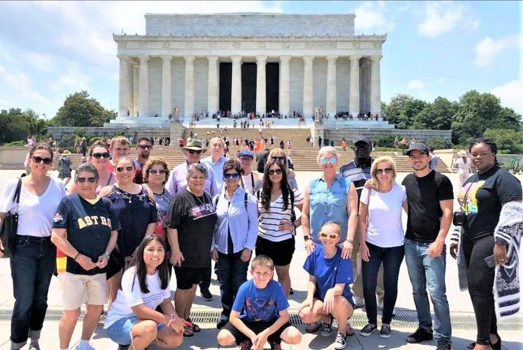 Group of people posing in front of the Lincoln Memorial on a sunny day.