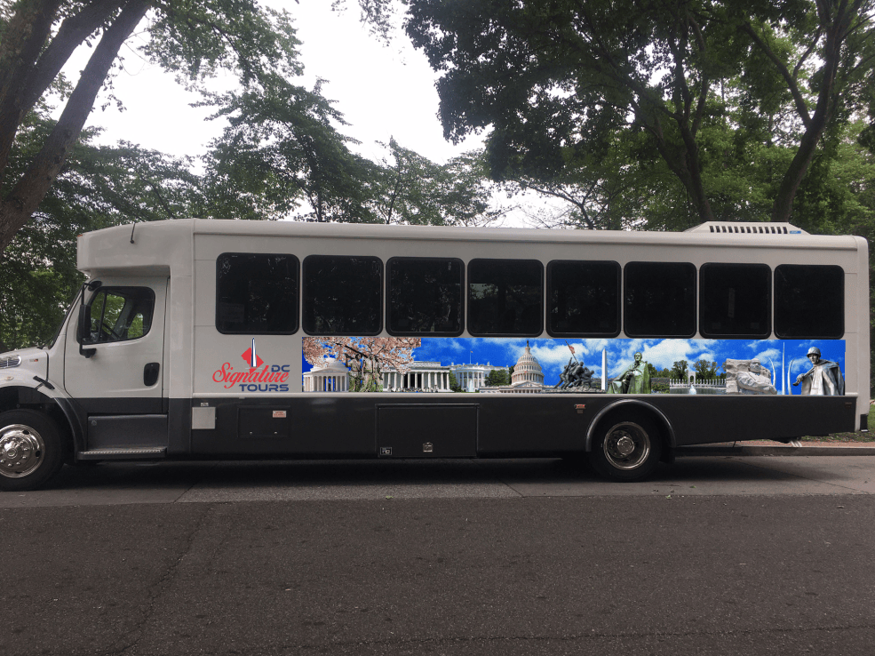 White tour bus with illustrations of D.C. monuments on the side, parked on a street.